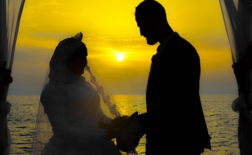 Silhouette of man and woman standing near body of water during sunset